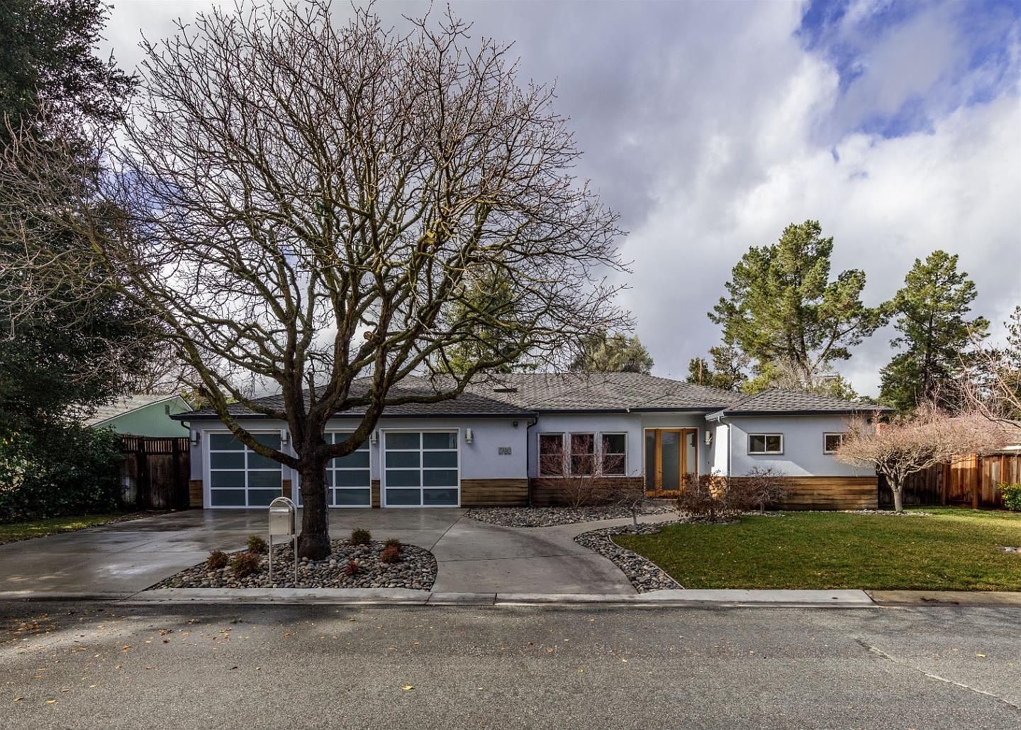 Three-quarter street view of 1677 Middleton, showing the renovated facade with frosted-glass garage doors, a wood-clad entry bay, and a clean concrete drive under an overcast sky