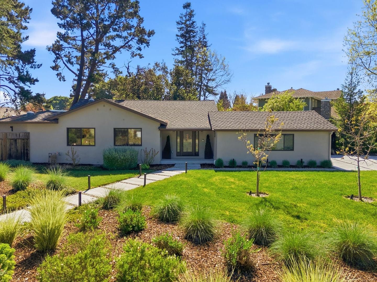Front elevation of 1677 Middleton Ave, a renovated single-level ranch with pale stucco, dark-framed windows, and native-grass landscaping under a clear Los Altos sky